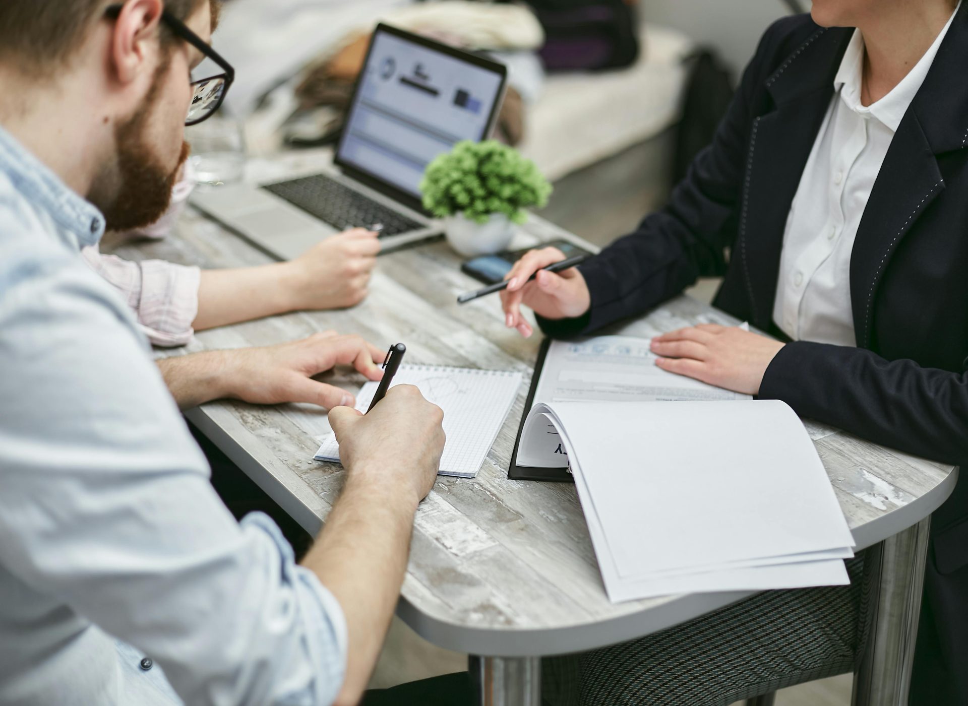 Colleagues collaborating and taking notes at a desk, discussing business documents.